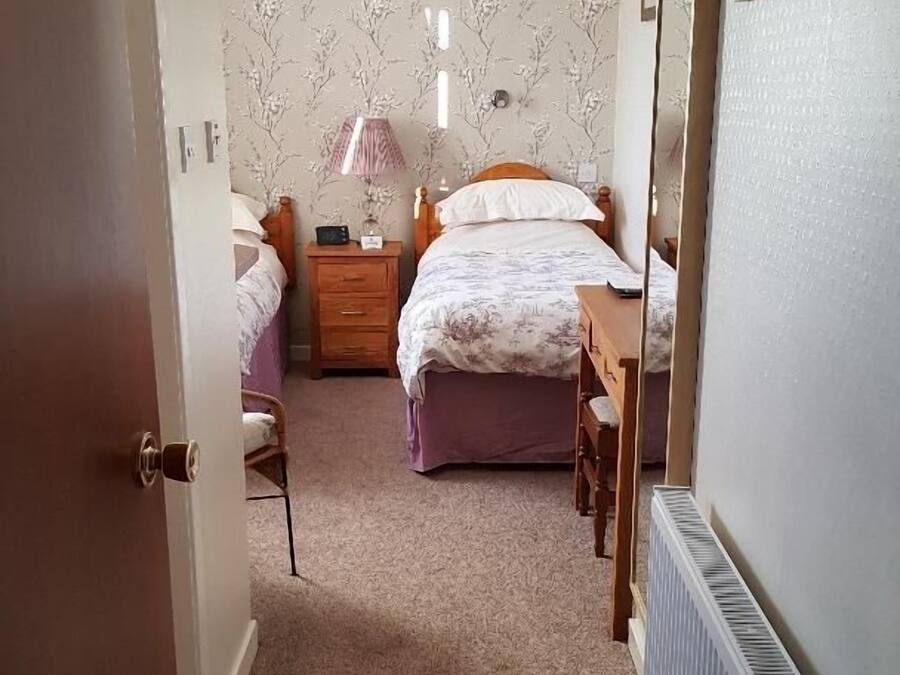 Ein Schlafzimmer mit einem Doppelbett, einem Nachttisch, einem Sessel, einem Heizkörper und einer Tür zu einem anderen Raum.