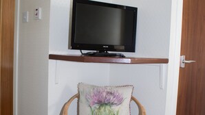 Ein Eckzimmer mit Fernseher, der über einem Korbsessel mit Blumenkissen auf einem Holzregal angebracht ist.