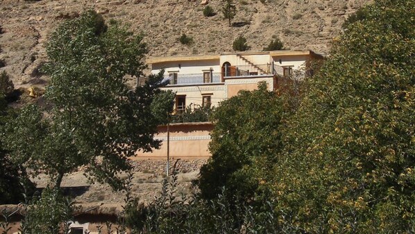 A building with a balcony, surrounded by trees and a rocky hillside. - Gite Paradis d'Ait Bouguemez - Hostel (Tabant)