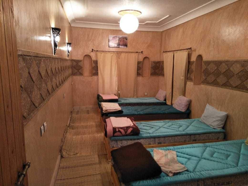 Une pièce avec quatre lits disposés en rangée, un luminaire au plafond et un tableau accroché au mur.