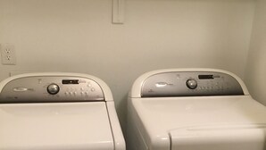 Dos lavadoras de carga frontal en un lavadero con una pared blanca y un enchufe eléctrico visible.