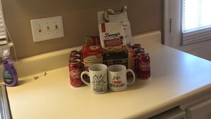 Una encimera de cocina con una cafetera, dos tazas y diversos alimentos.