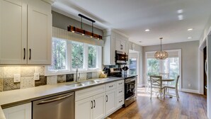 A modern kitchen with a central island, large windows, and a dining area with a chandelier. - Four Bedroom Sea Pines Home with Private Pool ~ 5 Minute Walk to the Beach! (Hilton Head Island)