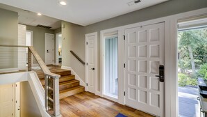 A spacious hallway with a wooden staircase leading to a second floor, white doors, and a view of the outdoors. - Four Bedroom Sea Pines Home with Private Pool ~ 5 Minute Walk to the Beach! (Hilton Head Island)