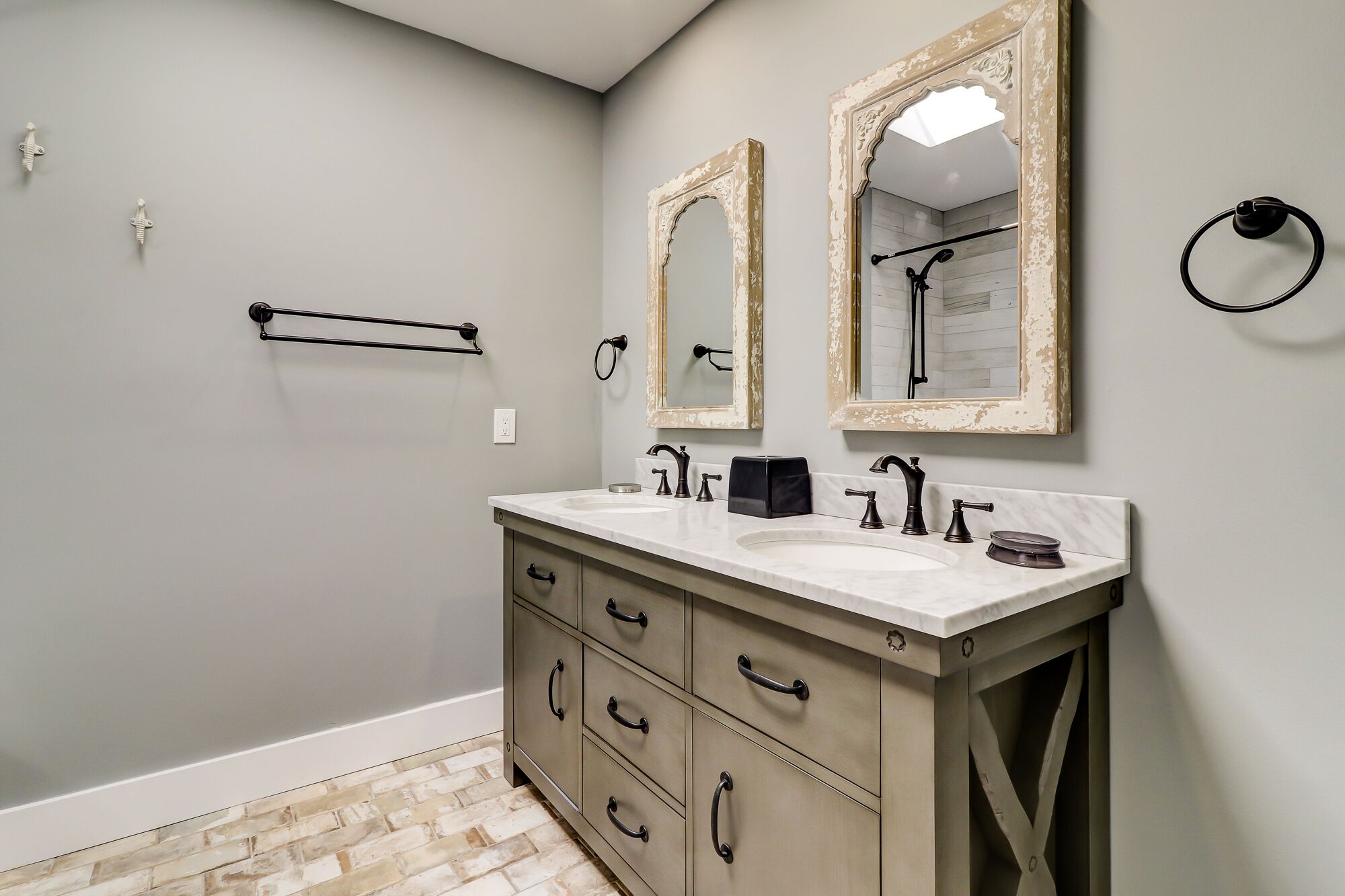 Une salle de bain avec un meuble-lavabo à deux vasques, deux miroirs, un porte-serviettes et un anneau pour suspendre les serviettes.