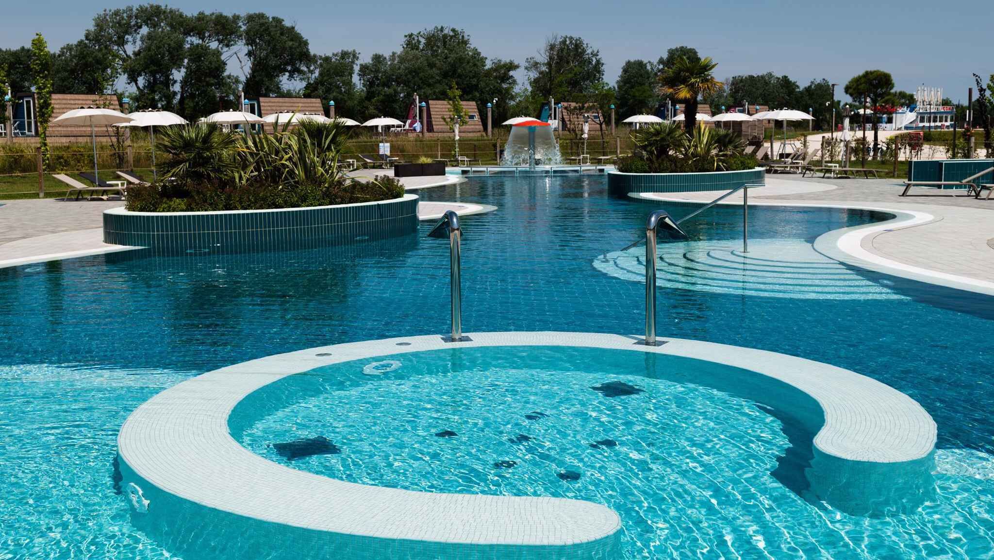 A large, circular pool with a central water feature and surrounding lounge areas.