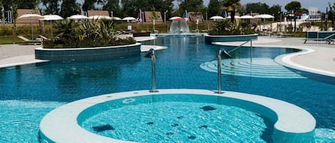 A large, circular pool with a central water feature and surrounding lounge areas.