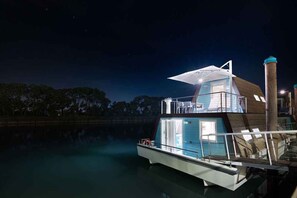 Una casa flotante con una terraza amplia y abierta, un nivel superior cubierto y una chimenea.