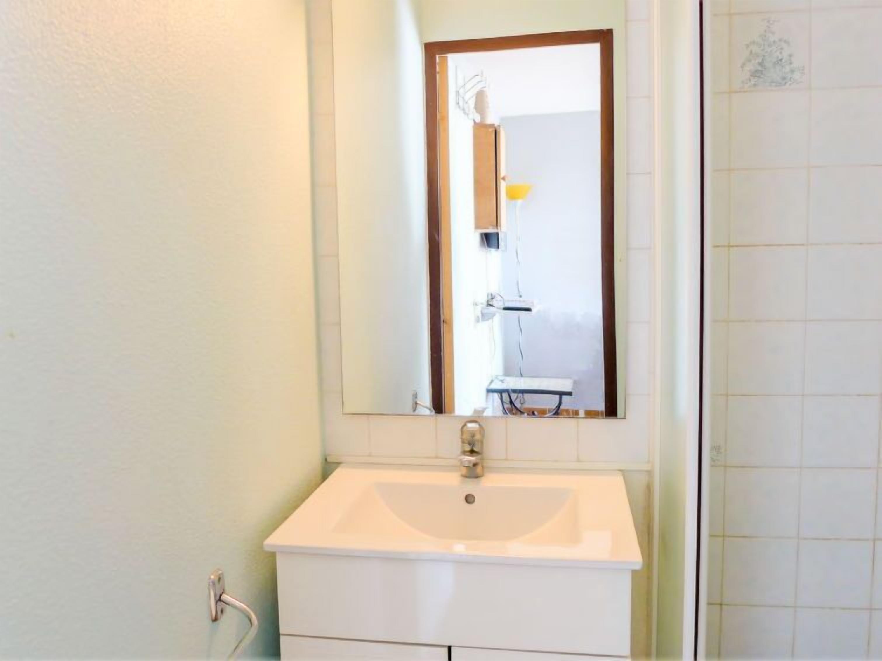 Casa de banho com lavatório branco, espelho e parede revestida a azulejos.