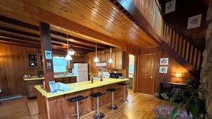 Ein Holzinterieur mit einer zentralen Barinsel, Barhocker, einem Kühlschrank und einer Mikrowelle.