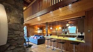 Ein gemütliches Interieur mit einer Steinwand, Holzbalkendecke, einer Couch, einem Essbereich mit Bar und einer Küche.