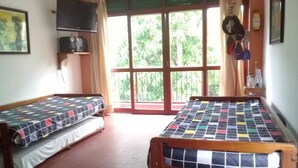 Ein Zimmer mit zwei Holzbett, einem an der Wand befestigten Fernseher und einem großen Fenster mit Vorhängen.