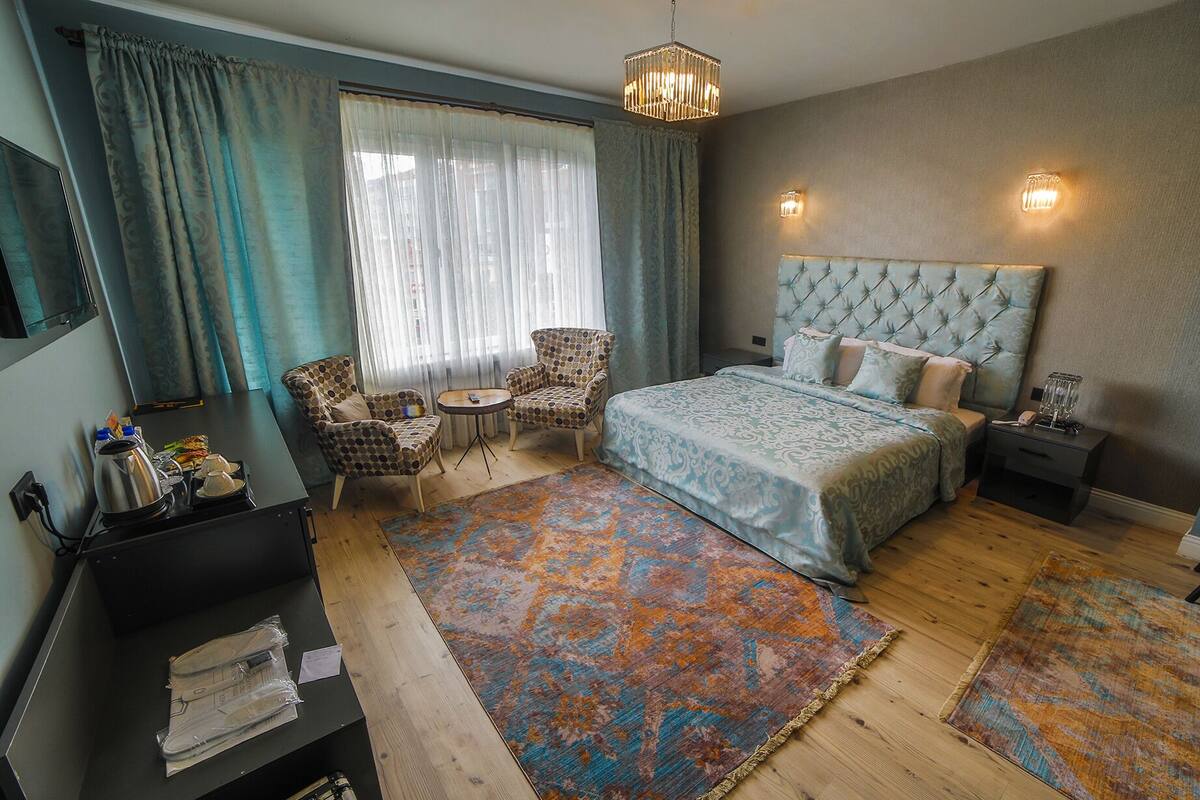 A bedroom with a bed, two armchairs, a small table, a nightstand, a lamp, and a decorative rug.