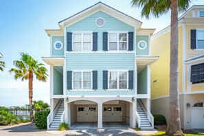 A two-story building with a light blue exterior, white trim, and dark blue shutters. It features a central entrance with a staircase and a garage with two doors.