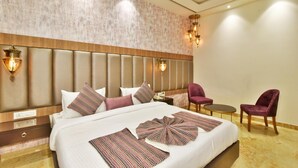 Habitación de hotel con una cama grande, cabecera con luces, una mesita pequeña, dos sillas y una mesita de noche.