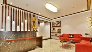 Un vestíbulo moderno con un mostrador de recepción de mármol, sofás rojos y una pared decorativa con listones verticales de madera y un emblema dorado.
