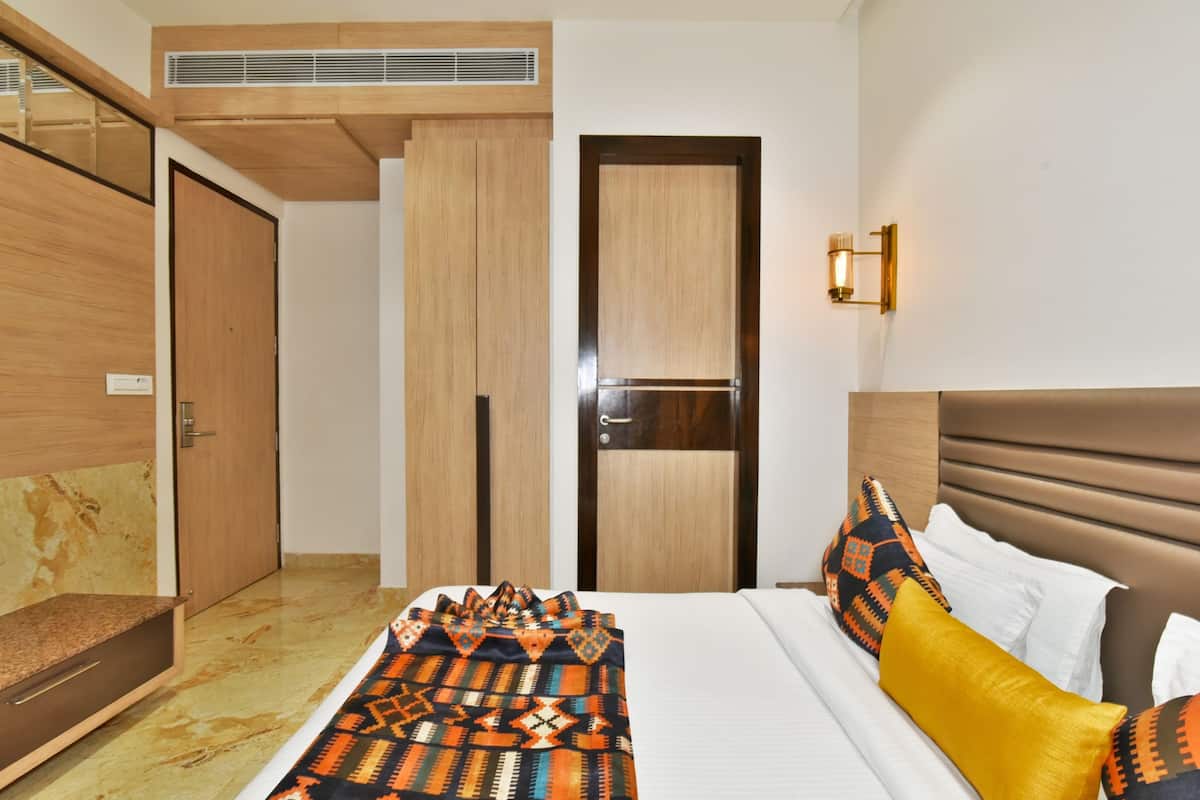A hotel room with a bed, a wardrobe, a mirror, and a wall-mounted light fixture.