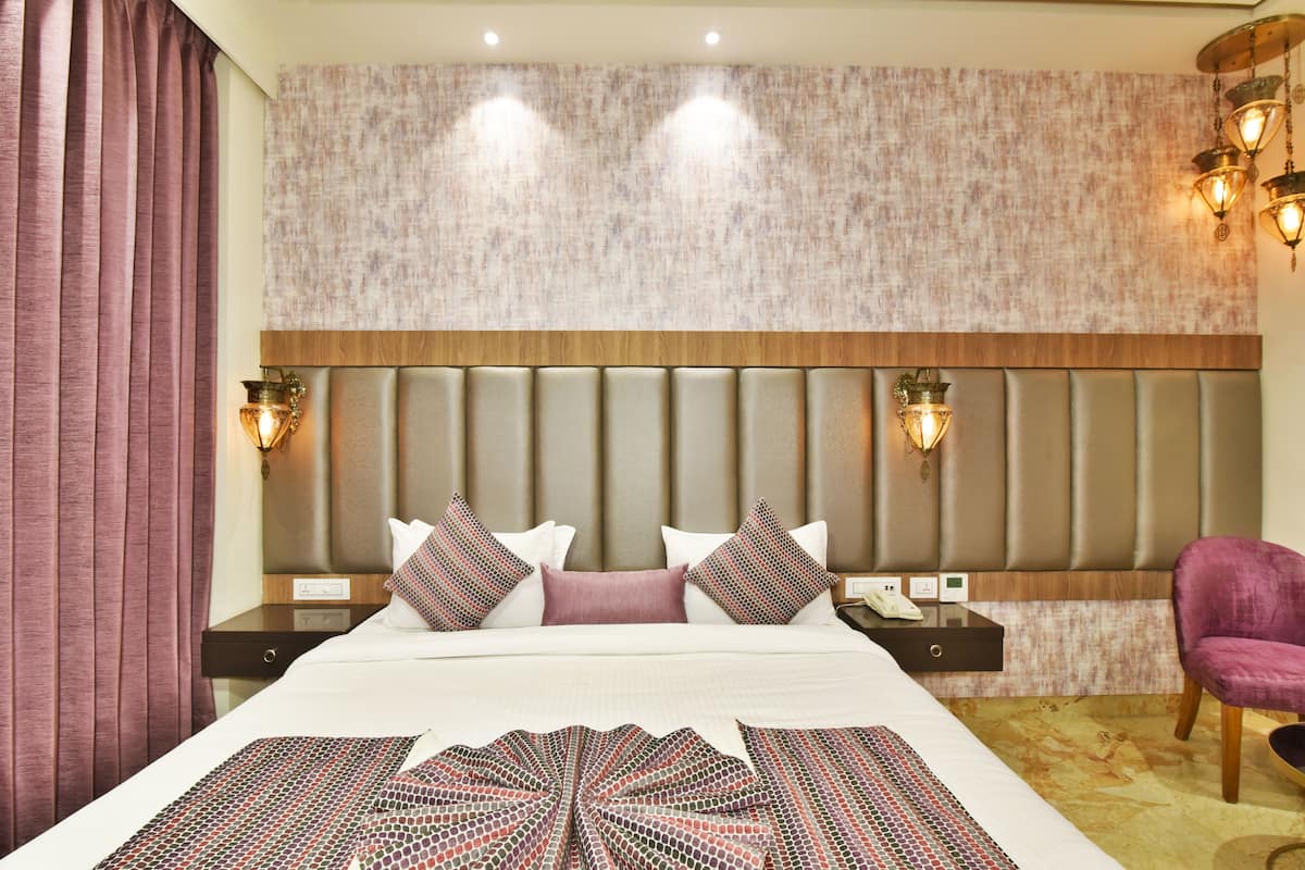 A hotel room with a large bed, a headboard with vertical panels, two bedside tables with lamps, a nightstand, and a chair.