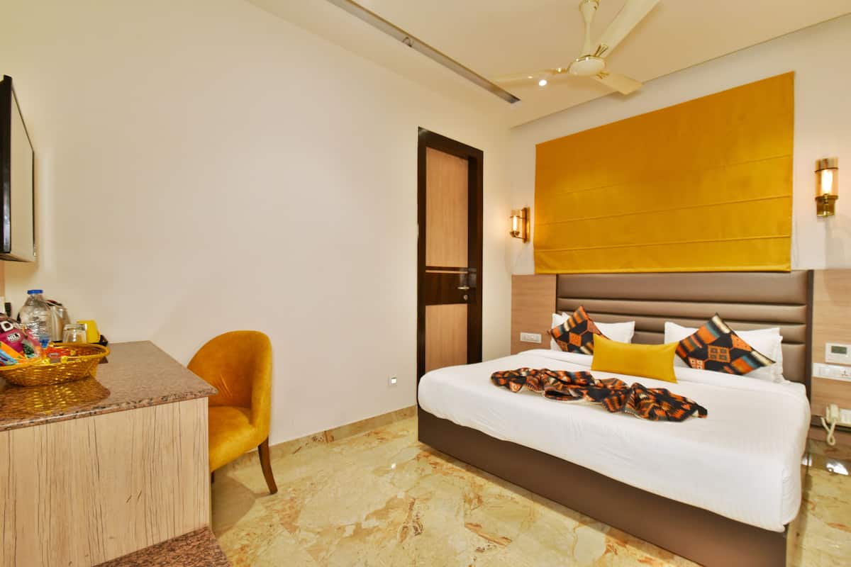 A hotel room with a bed, a desk, a chair, a television, and a wall-mounted light fixture.
