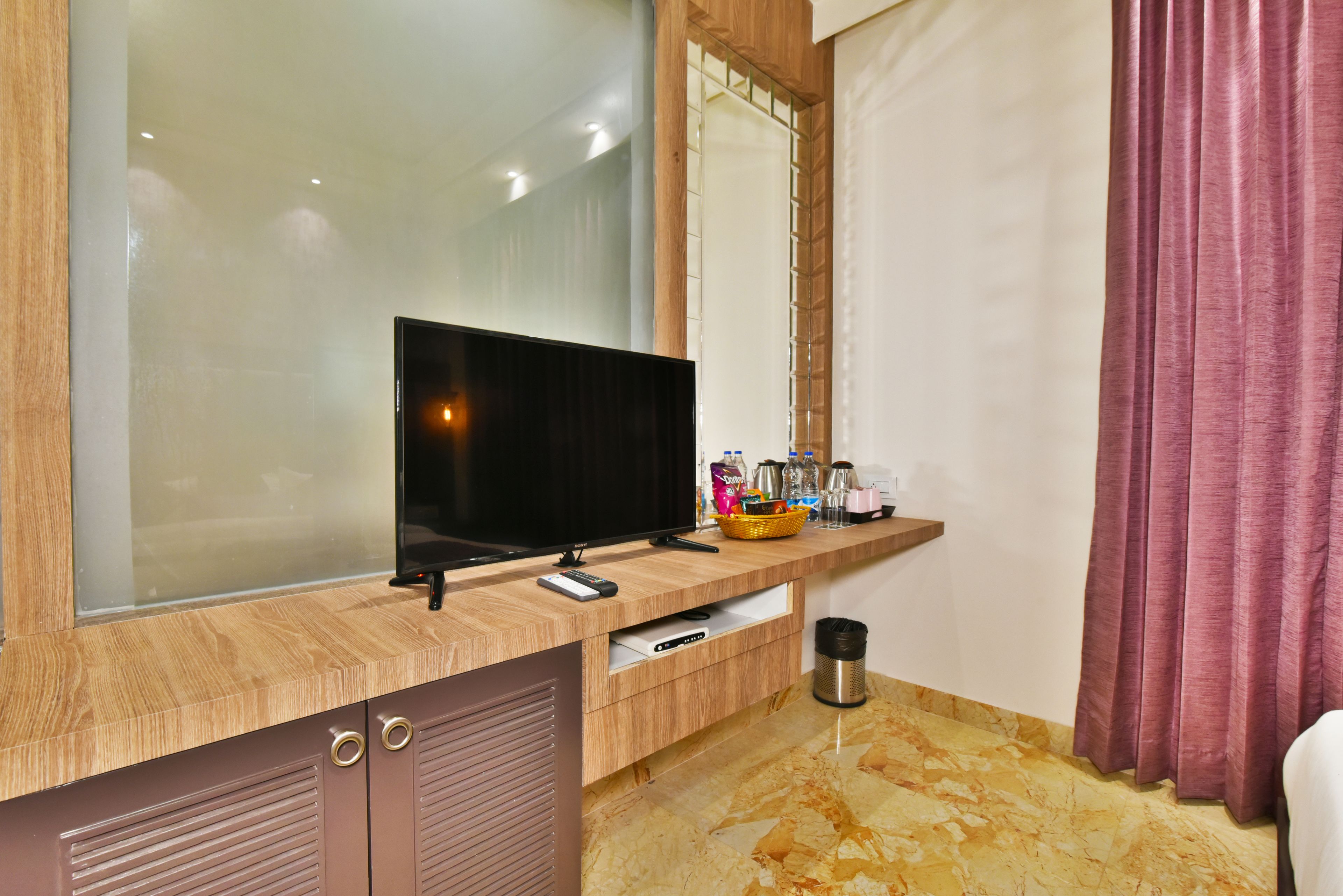 A modern bathroom with a wooden vanity, a mirror, a television, and a trash bin.