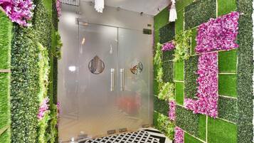 Un interior moderno con una puerta de cristal, decoraciones florales rosa y verde en la pared, y un suelo con estampado geométrico.