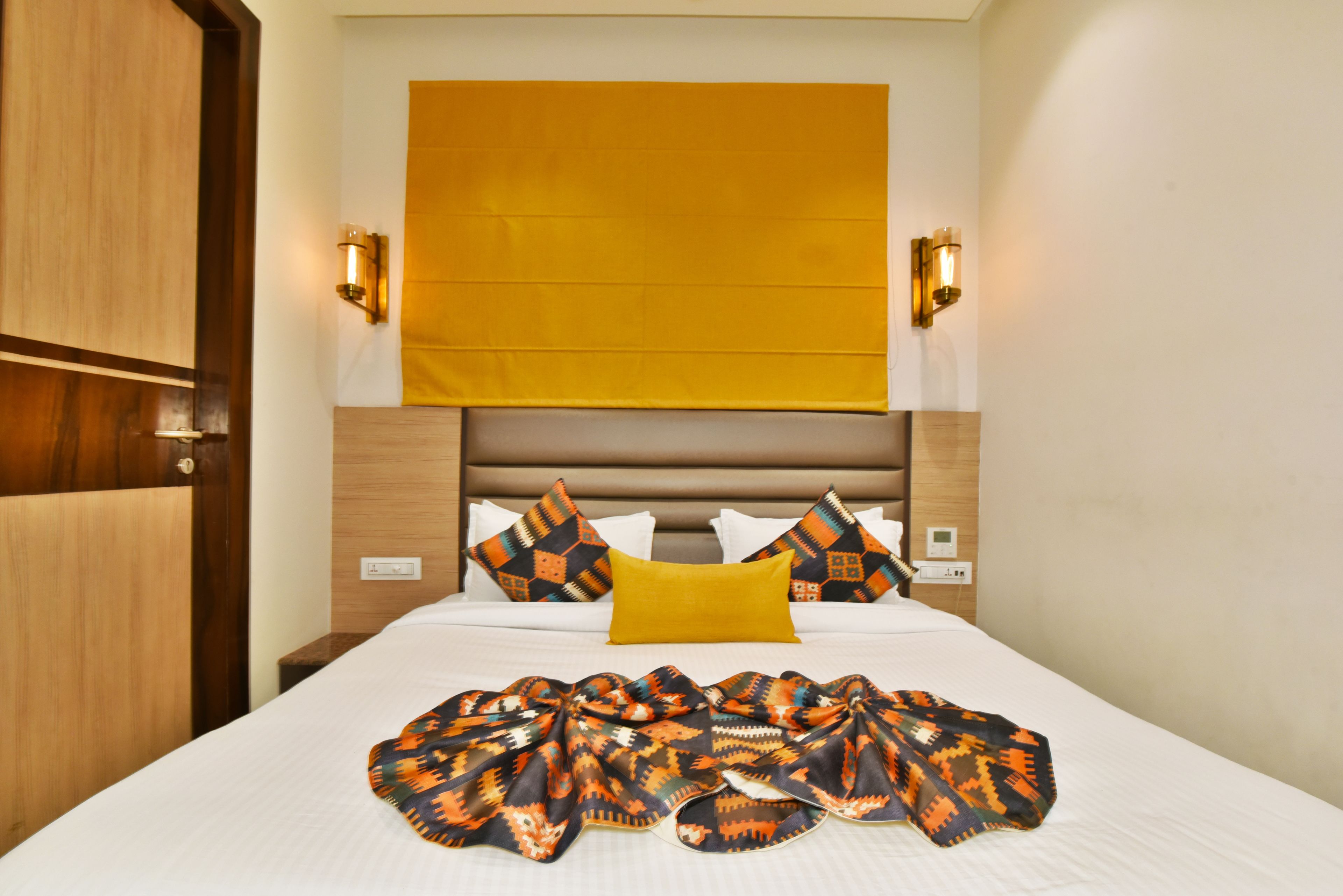 Une chambre d’hôtel avec un lit, une porte en bois et un luminaire fixé au mur.