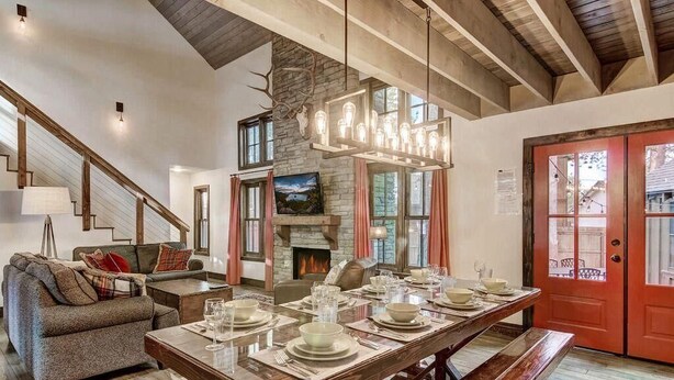 A spacious dining area with a long wooden table set for a meal, a stone fireplace, and a staircase leading to another level. - Heavenly Hideaway 4BR,4BA, Hot Tub (South Lake Tahoe)