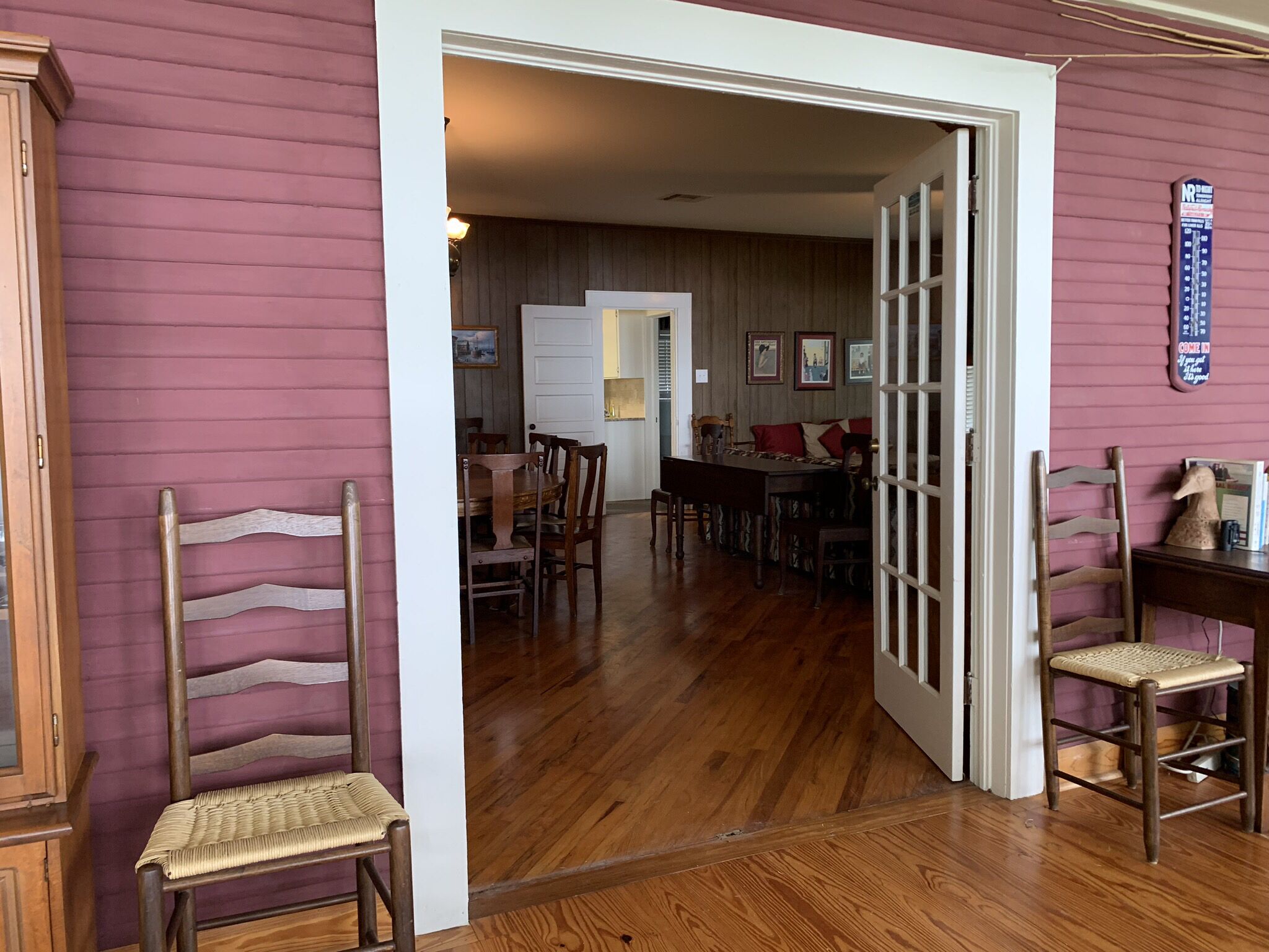 A wooden dining table with chairs in a room with wooden floors and a pink wall.