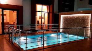 An indoor swimming pool with a glass barrier, wooden flooring, and a wall with a textured light feature. - Sawsana Villalari (Sapanca)