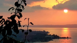 A sunset over a body of water with a distant shoreline and vegetation in the foreground. - Sawsana Villalari (Sapanca)