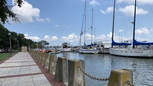 Ein Yachthafen mit vor Anker liegenden Booten, eine Promenade mit Backsteinpflaster und einem wolkenlosen Himmel.