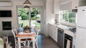 Una cocina moderna con armarios blancos, un comedor con una mesa de madera y sillas blancas, y vistas a un jardín a través de un ventanal.