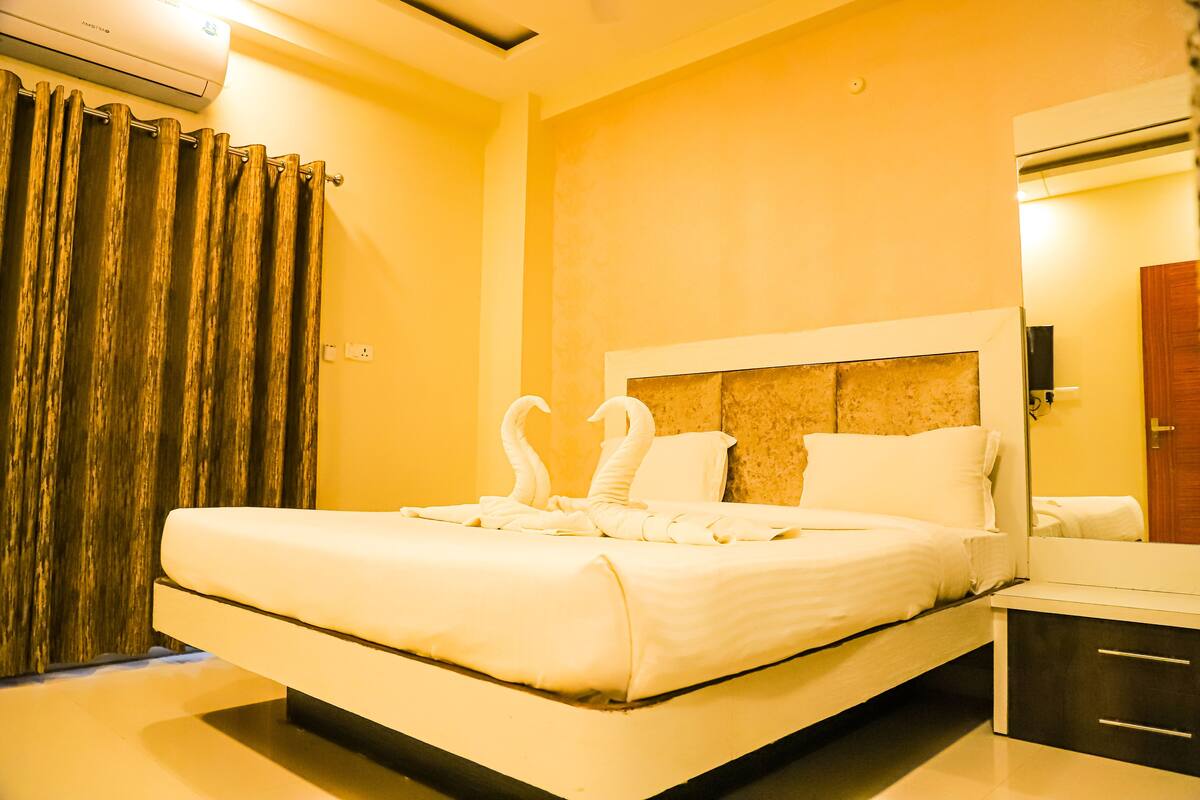 A hotel room with a large bed, a headboard, a bedside table, a mirror, and an air conditioning unit.
