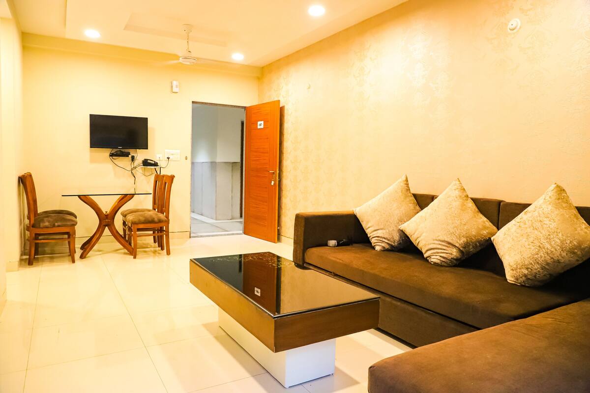 A living room with a sofa, two armchairs, a coffee table, a TV, and a door leading to another room.