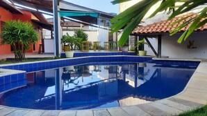 A swimming pool with blue tiles, surrounded by a patio area with plants and outdoor furniture. - Pousada Villa Tropicale (Salvador)