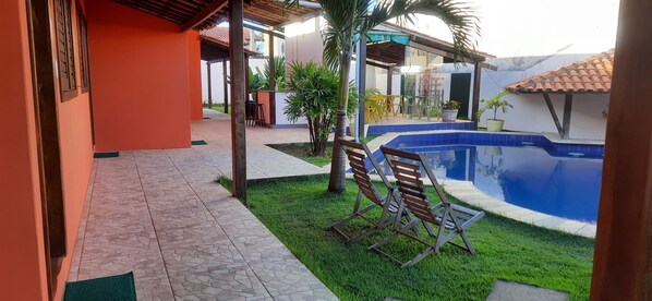 A covered outdoor area with a swimming pool, seating, and a small garden.