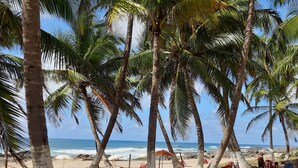 A beach with palm trees, red plastic chairs, and a wooden table. - Pousada Villa Tropicale (Salvador)