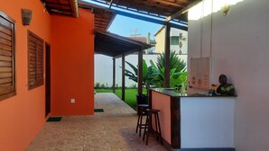 A corridor with a tiled floor leading to a covered outdoor area with a bar and stools. - Pousada Villa Tropicale (Salvador)