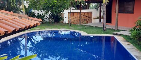 A swimming pool with tiled edges, surrounded by greenery and a building with a tiled roof.