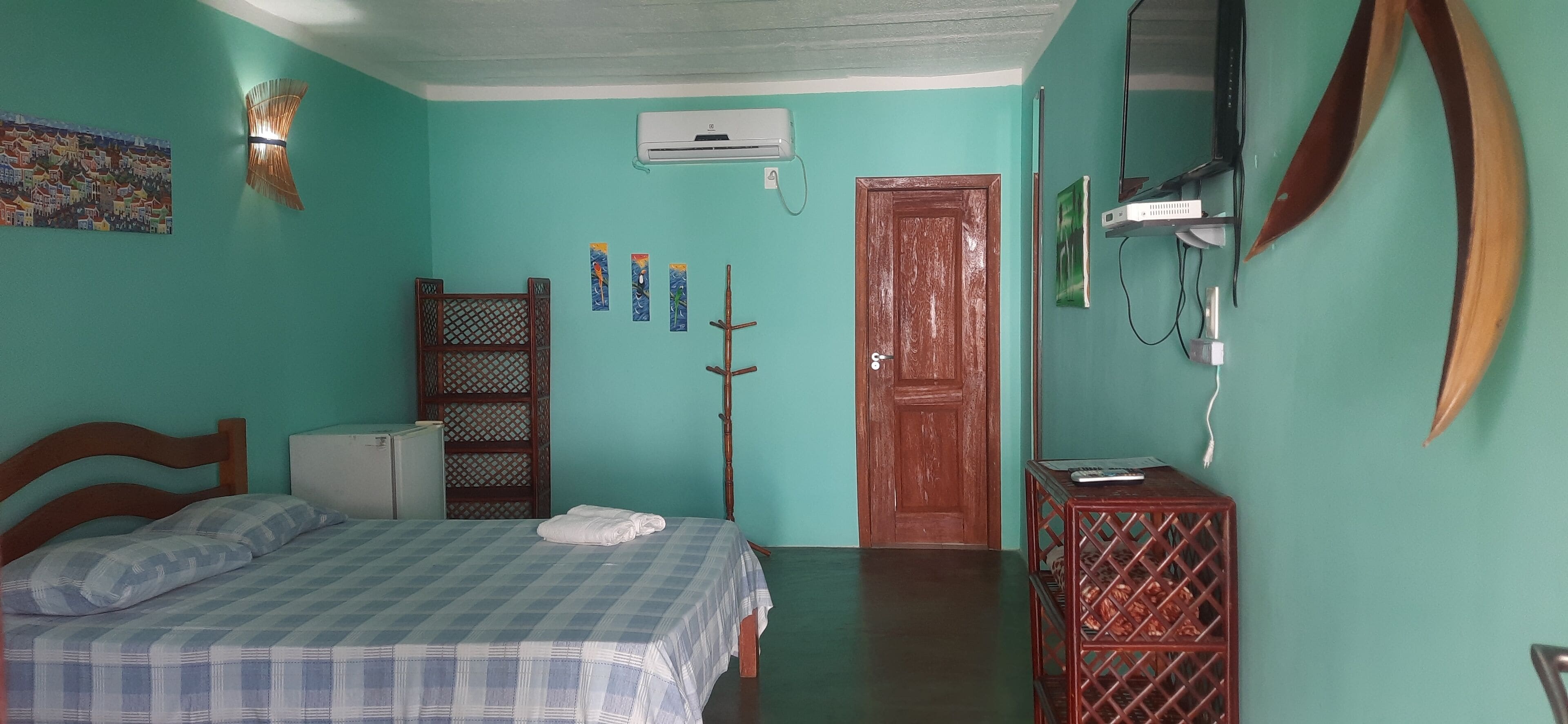 A room with a bed, a wardrobe, a door, and a small table with a remote control.