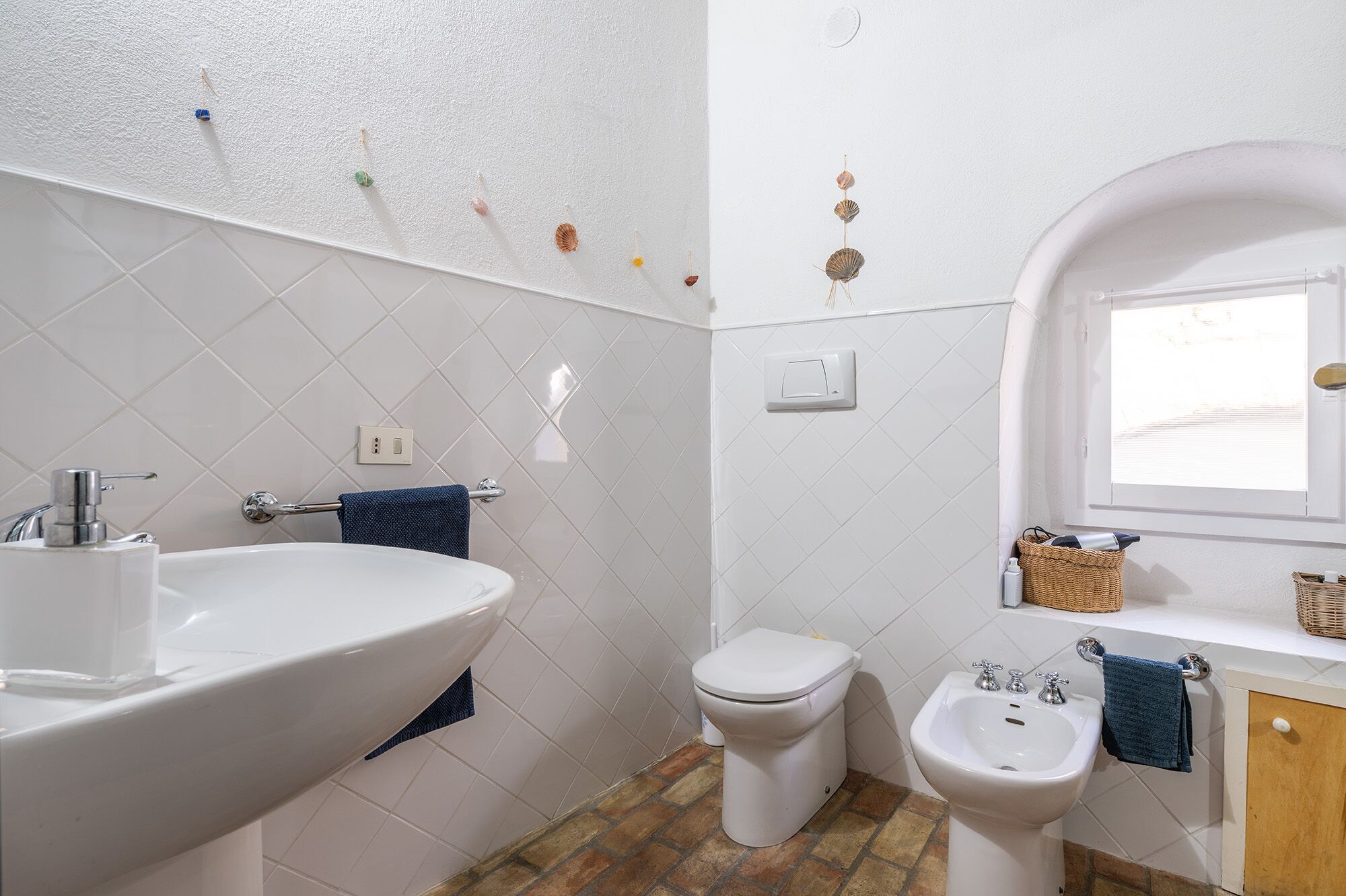 Et badeværelse med vask, toilet, bidet og et vindue.