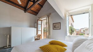 A bedroom with a bed, a window with a view of buildings, a white wardrobe, and a wooden ceiling. - Meigama, modern loft in historic center of Cagliari (Cagliari)