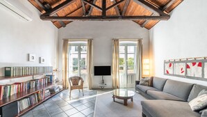 A spacious living room with a high ceiling, a bookshelf, a sofa, and a television. - Meigama, modern loft in historic center of Cagliari (Cagliari)