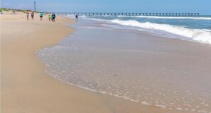 A beach with a pier extending into the water, people walking along the shore, and a clear sky. - 360' to Beach Access - 1500' to Community Pool/Courts (Duck)