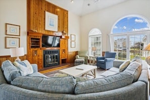 A living room with a fireplace, a large window, and a sofa. - 360' to Beach Access - 1500' to Community Pool/Courts (Duck)
