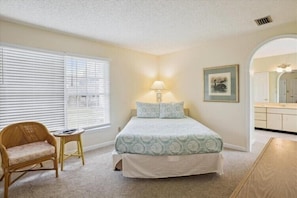 A bedroom with a bed, a chair, a small table, and a window with blinds. - 360' to Beach Access - 1500' to Community Pool/Courts (Duck)