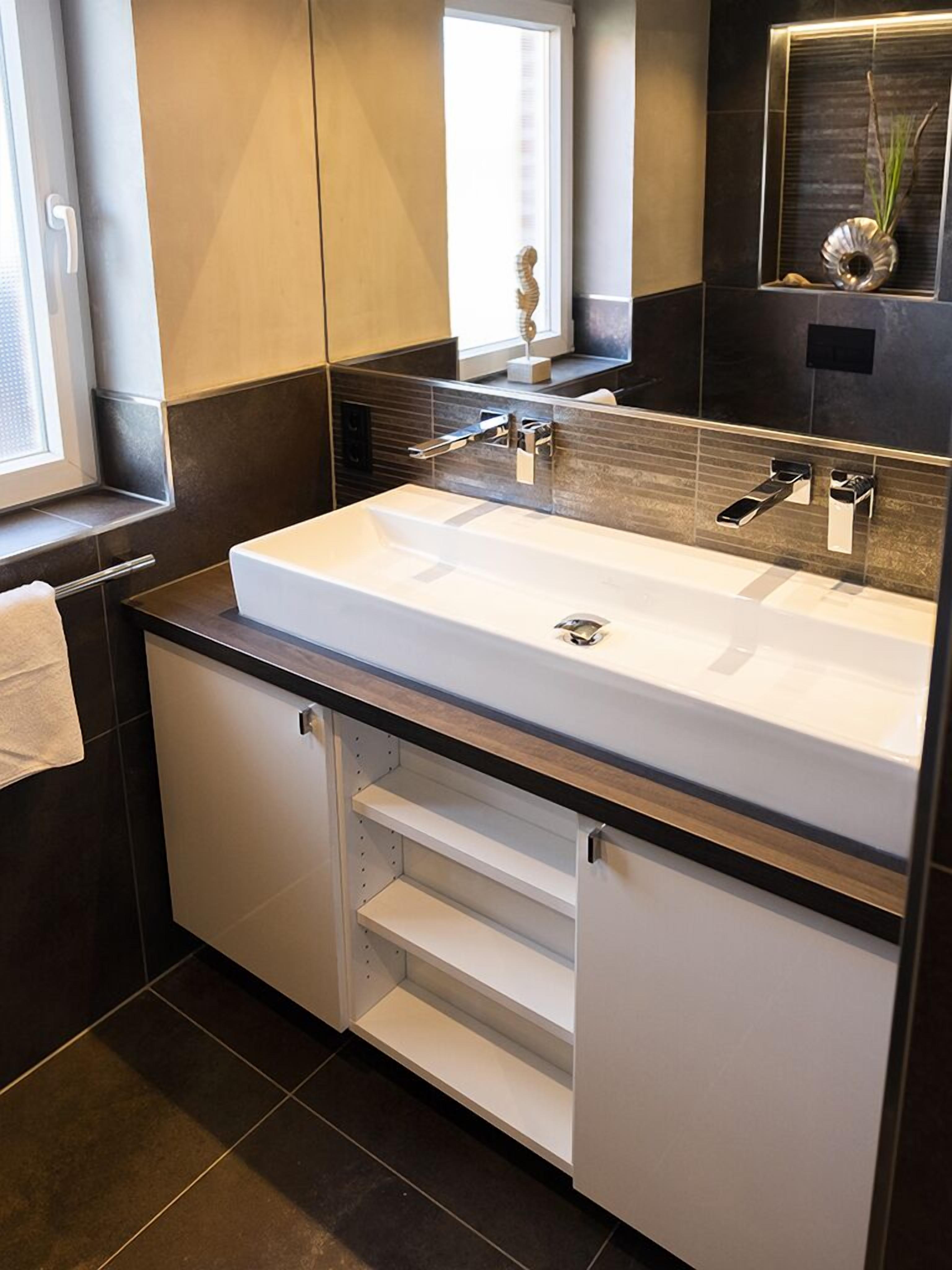 A modern bathroom with a large white sink, dark tiles, and a mirror above it.