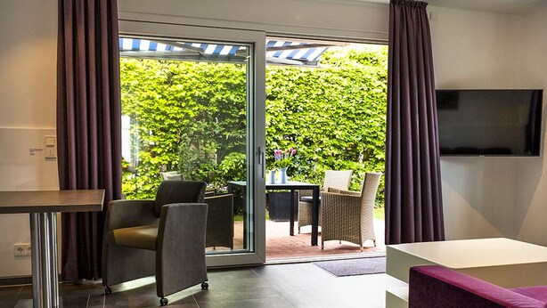 Een moderne kamer met een schuifdeur naar een buitenruimte, een wandgemonteerde flatscreen televisie en een eettafel met stoelen.