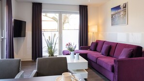 Een moderne woonkamer met een paarse bank, een flatscreen televisie, een salontafel en een eethoek met een tafel en stoelen.