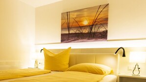 Hotelkamer met een bed, nachtkastje, lamp en een schilderij van een zonsondergang boven het gras.